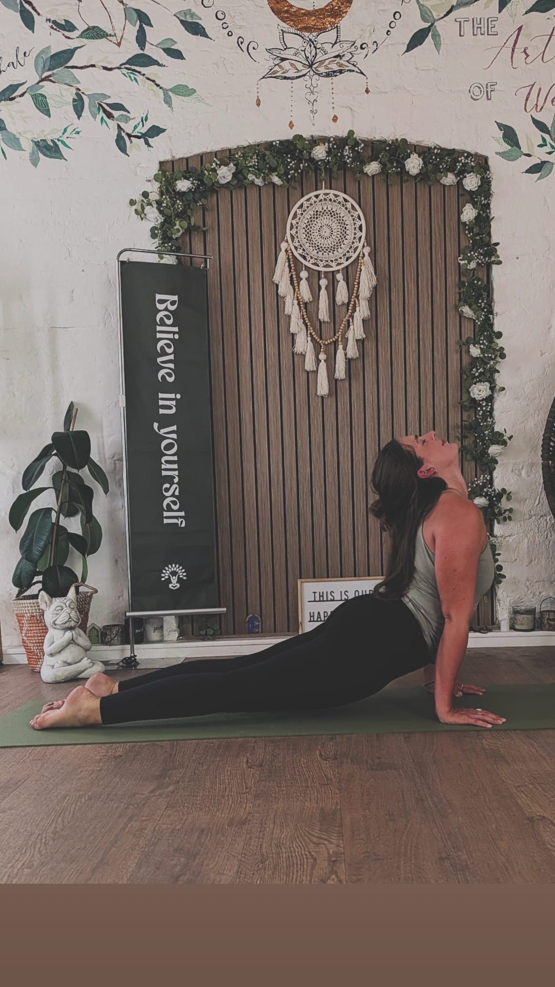 Han practising on a green mat, chest lifted, beneath the dream catcher
