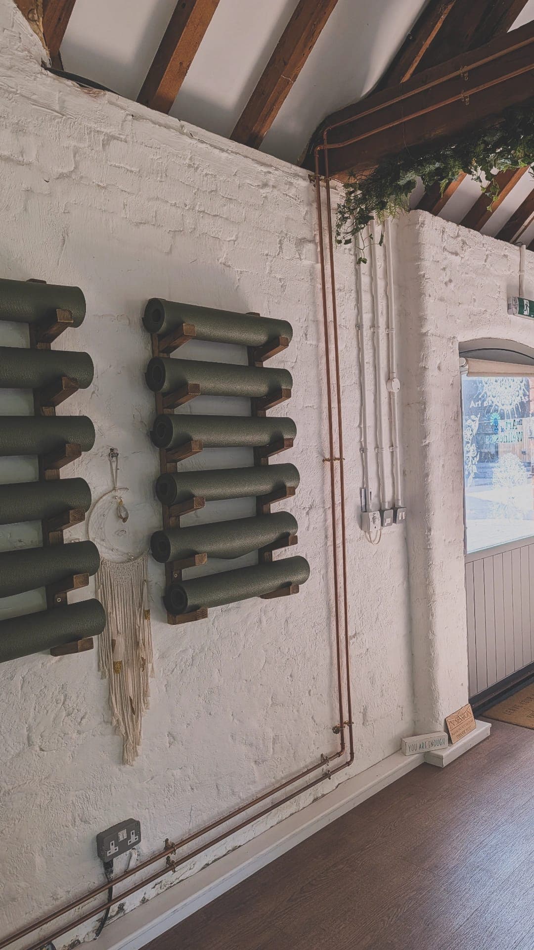 Rolled green mats on wooden racks against the white brick wall of the studio